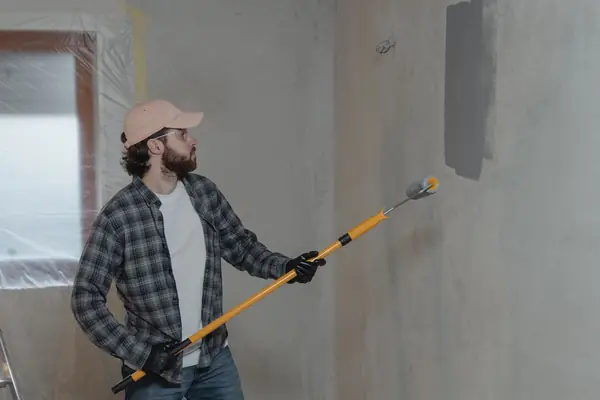 Painter rolling grey paint onto an interior wall in Fremont